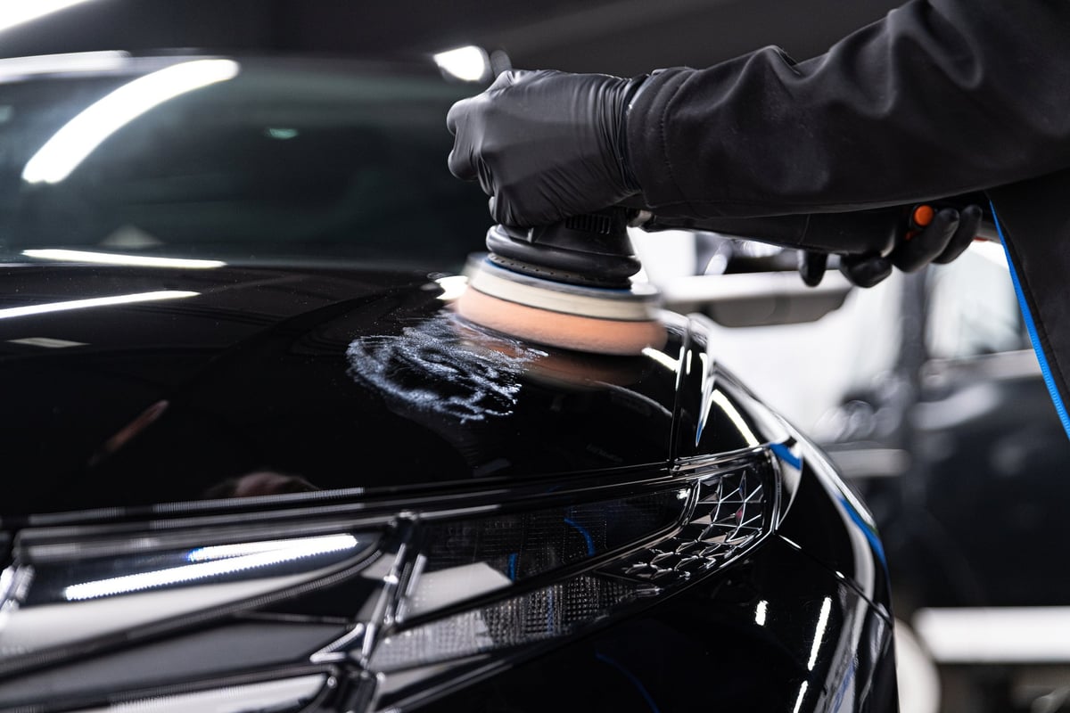 Man worker of car detailing studio removing scratches on car varnish with electric polisher