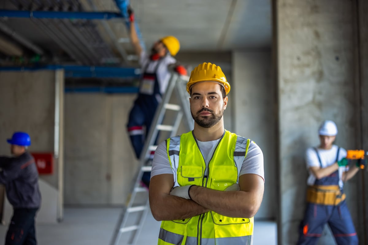 Portrait of serious male worker wearing fluorescent yellow vest and hard hat standing with arms crossed on site